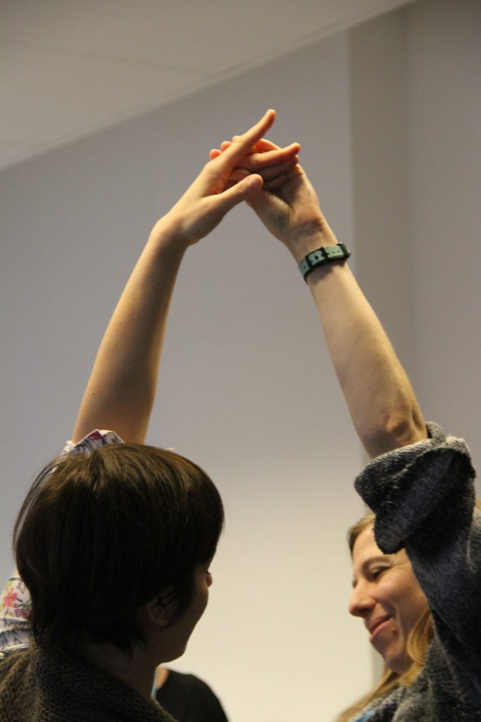 two people smiling with one arm each above their heads, hands clasped together